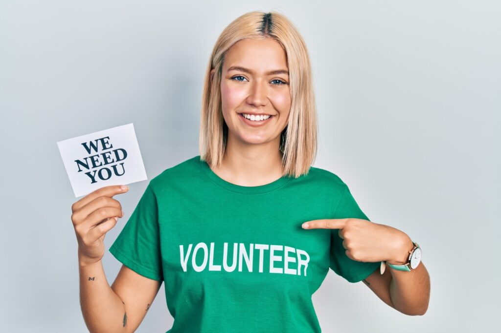 Woman wearing volunteer t shirt showing we need you banner.