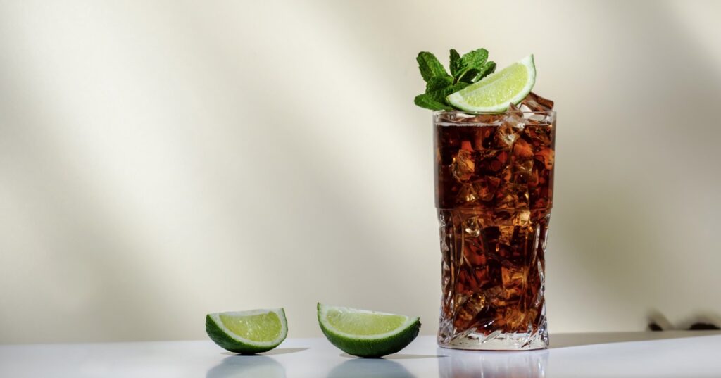 Whiskey cola cocktail with strong alcohol and ice, garnished with mint and lime in highball glass is a drink idea for a day at the races fundraiser theme.