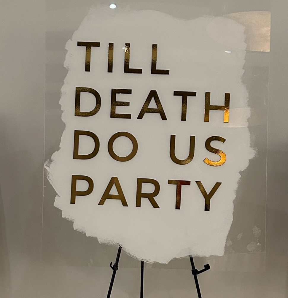 A sign on a stand saying til death do us party is a great wedding theme fundraiser venue decor idea
