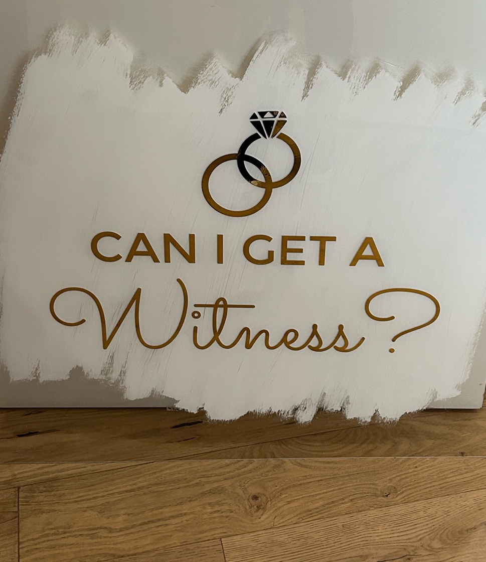 A sign with gold text and rings on it saying can i get a witness is a great wedding theme fundraiser venue decor idea