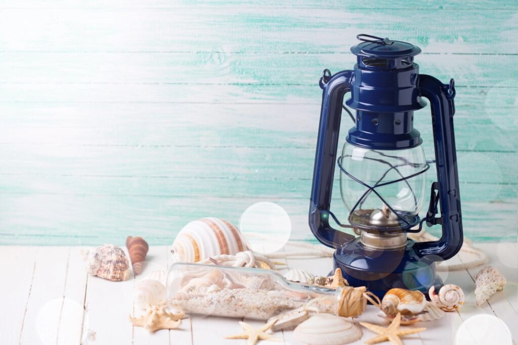 A blue lantern and seashells on a white surface for a Sand and Sea Fundraiser decor idea